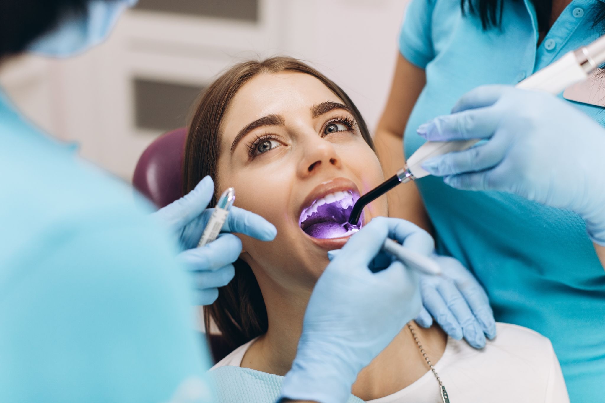 Woman receiving light-curing treatment for a dental filling from a dentist and dental assistant