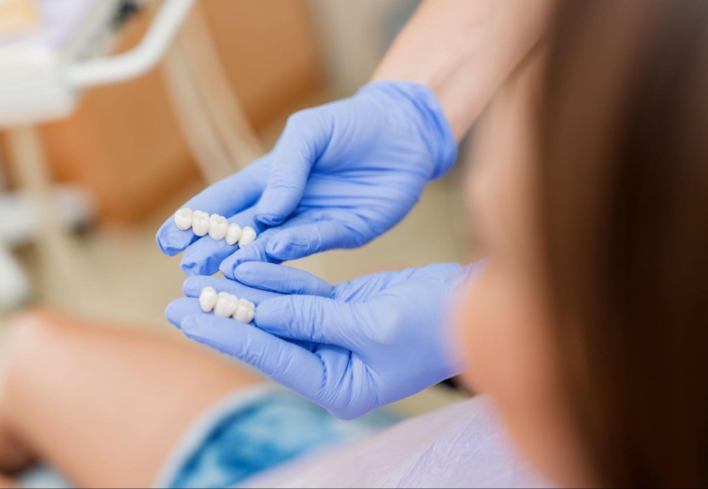 Dentist holding dental bridges while showing it to a patient